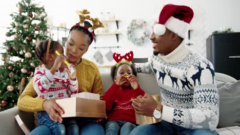 Porträt-Neugieriger-Kinder-öffnen-Geschenkboxen,-Während-Sie-Mit-Glücklichen-Eltern-Zusammen-In-Einem-Geschmückten-Haus-In-Der-Nähe-Eines-Hübschen-Weihnachtsbaums-An-Silvester-Sitzen