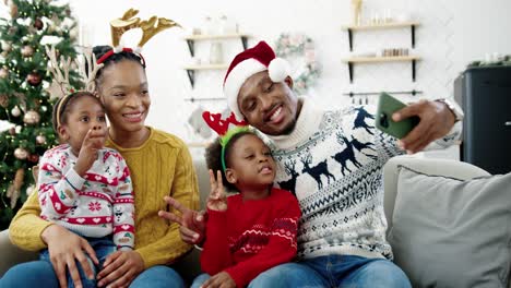 Porträt-Einer-Glücklichen-Familie,-Die-Fotos-Auf-Dem-Smartphone-Macht-Und-In-Einem-Gemütlichen,-Weihnachtlich-Dekorierten-Haus-Lächelt