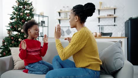 Portrait-Of-Happy-Beautiful-Woman-Playing-With-Little-Kid-While-Sitting-On-Sofa-In-Christmassy-Decorated-Room-Side-View-Of-Loving-Mom-And-Child-Spending-Time-Together-Holidays-Concept