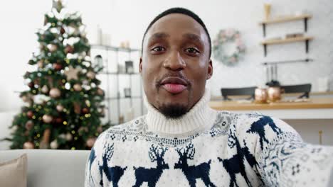 Pov-Of-Happy-Handsome-Male-In-Xmas-Sweater-Videochatting-While-Sitting-Near-Decorated-New-Year-Tree-At-Home