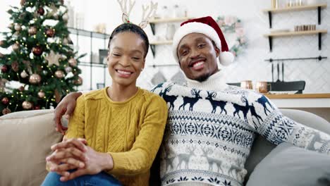 Portrait-Of-Happy-Married-Couple-Sitting-In-Room-With-Decorated-Glowing-Christmas-Tree,-Looking-At-Camera-And-Smiling-In-Good-Xmas-Mood