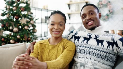 Close-Up-Portrait-Of-Happy-Married-Couple-Man-And-Woman-Sitting-In-Room-With-Decorated-New-Year-Tree,-Looking-At-Camera-And-Smiling-In-Good-Xmas-Mood