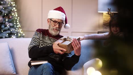 Happy-Cute-Little-Girl-And-Boy-Giving-Presents-To-Old-Grandpa-While-Sitting-At-Cozy-Decorated-Home-Near-New-Year-Tree-And-Reading-Book