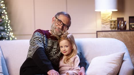 Portrait-Of-Loving-Caring-Old-Grandfather-In-Glasses-Spending-Christmas-Eve-Together-With-Joyful-Grandchild-Sitting-In-Decorated-House-Near-Xmas-Tree-Embracing-Together