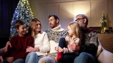 Portrait-Of-Happy-Family-Gathering-Together-At-Cozy-Home-Near-Decorated-Glowing-Xmas-Tree-Chatting,-Smiling-And-Making-Jokes-On-Christmas-Eve-In-Evening