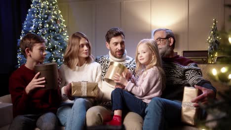Fröhliche-Familie-Mit-Kindern,-Die-In-Einem-Gemütlichen-Zuhause-In-Der-Nähe-Des-Geschmückten-Weihnachtsbaums-Zusammensitzen,-Lächeln-Und-Sich-Am-Silvesterabend-Weihnachtsgeschenke-Und--geschenke-Geben