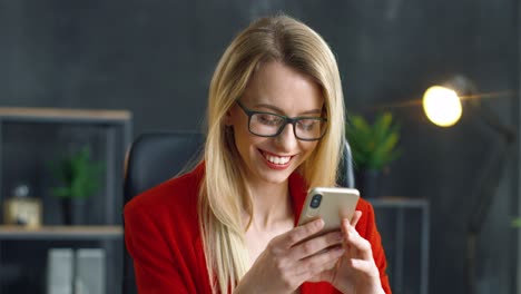 Blonde-Businesswoman-In-Glasses-Holding-Smartphone-In-Hands-In-The-Office