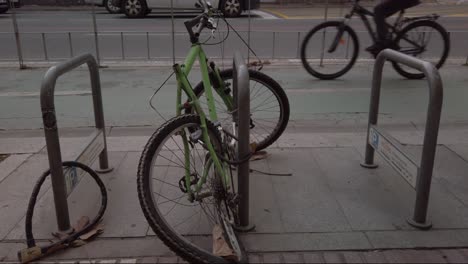 Vandalized-bike-with-bent-wheel-locked-by-bicycle-lane-as-cyclists-pass,-SLOWMO