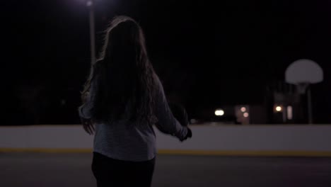 Low-angle-tight-shot-of-teenage-girl-dribbling-basketball-then-taking-a-shot-at-an-outdoor-court-at-night-with-lights