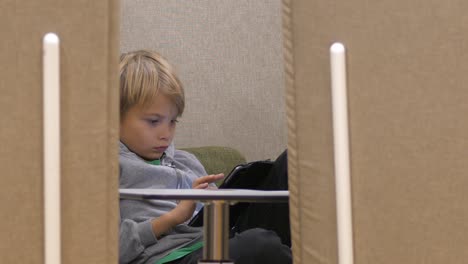 School-boy-studying-on-a-tablet-seen-through-a-gap-of-cozy-sofas,-Static