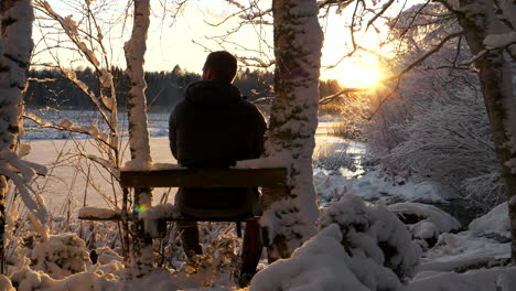 Lone-man-relaxing-in-snowy-winter-wonderland-enjoying-golden-sunset