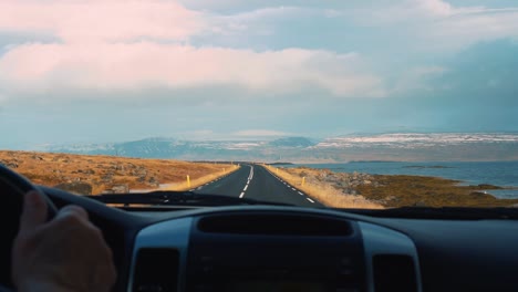 Driving-on-the-road-by-a-lake-in-Iceland-with-icy-mountains-in-the-distance---slowmo