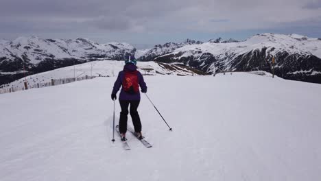 Un-Plano-Siguiendo-A-Una-Mujer-Esquiando-Por-Una-Pendiente-Con-Unas-Montañas-Al-Fondo