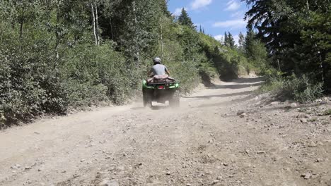 Slow-motion-shot-of-an-ATV-Rider-driving-his-quad-on-a-dirt-path-in-the-mountains,-leaving-a-large-dirt-cloud-behind-him