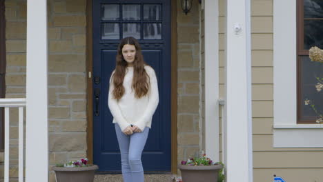 Girl-standing-on-porch-at-home-looks-into-camera,-medium-shot