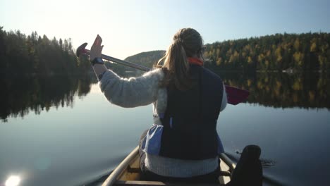 Woman-paddling-canoe-boat-on-beautiful-lake-in-autumn,-rear-view-slow-motion