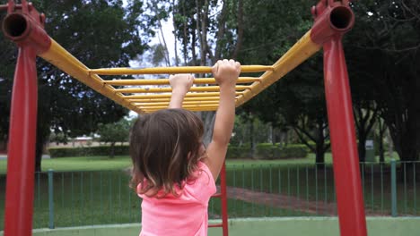 Four-year-old-girl-playing-in-the-jungle-gym-hanging-from-the-bars-showing-great-skill-and-ability