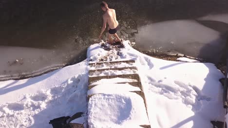 Man-standing-on-snow-covered-steps-leading-to-frozen-lake-with-small-area-of-broken-ice