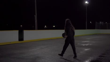 Teenage-girl-with-brown-hair-and-black-sweater-shoots-basketball-in-at-outdoor-court-in-the-dark-with-lights
