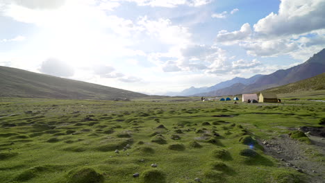 Handheld-shot-as-walking-around-a-tent-camp-in-the-mountains-on-a-sunny-day,-on-an-open-green-field-with-grass