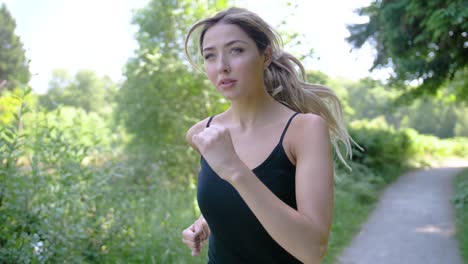 A-pretty-young-woman-concentrates-as-she-runs-on-a-park-path-near-a-pond