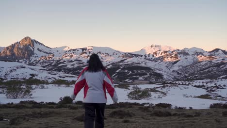 Women-in-a-winter-clothing-walking-towards-snow-covered-mountains-at-dusk