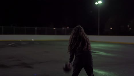 Teenage-girl-dribbles-ball-then-shoots-it-at-net-at-an-outdoor-court-at-night