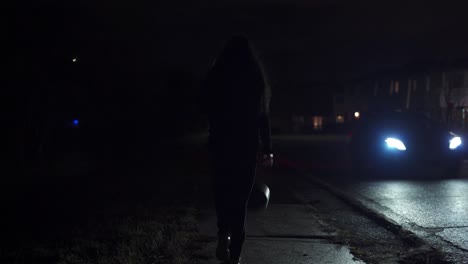Teenage-girl-dribbling-basketball-down-sidewalk-of-suburban-street-with-car-passing-at-night