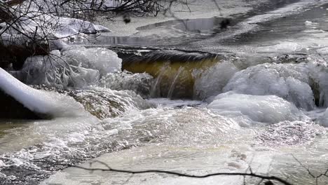 Gezoomt-Im-Hinblick-Auf-Den-Zugefrorenen-Fluss,-Der-In-Zeitlupe-über-Eisbedeckte-Felsen-Fällt