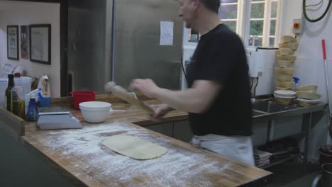 Man-working-with-dough,-using-rolling-pin-on-wooden-counter-top