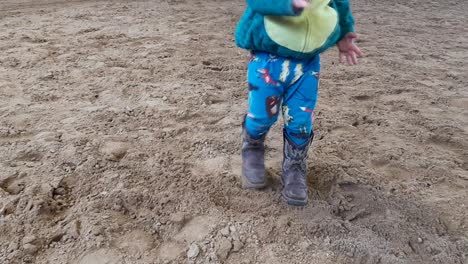 Kind-In-Dinosaurierkostüm-Und-Cowboystiefeln,-Die-Im-Sand-Spielen