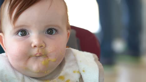 A-mother's-hand-scooping-up-baby-food-off-of-a-toddlers-face-with-a-spoon,-Front-facing-shot---slow-motion