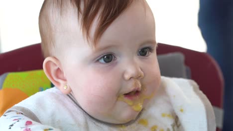 A-toddler-in-its-seat-eating-its-baby-food-in-slow-motion,-close-up-shot