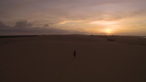 Aerial-shot-of-a-young-guy-running-towards-the-sunset-in-a-desert