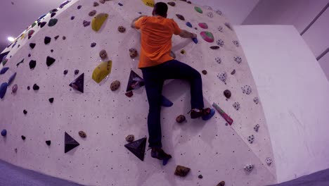 Boulder-gym-climbing-wall-seen-from-below-as-a-climber-approaches-and-climbs-up-and-then-down-with-no-rope