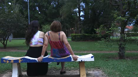 Mother-and-daughter-sitting-on-a-bench-in-the-park-talking-to-each-other-and-chilling-down-with-a-subtle-sliding-camera-movement