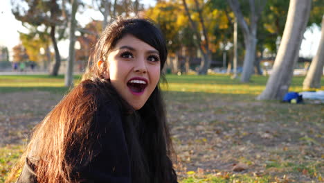 A-cute-girl-sitting-in-a-park-with-autumn-leaves-looking-up-with-a-surprised-shocked-look-and-then-laughing-in-slow-motion