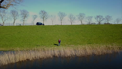 Aerial-drone-shot-of-flying-forward-to-the-adult-woman-standing-near-the-lake
