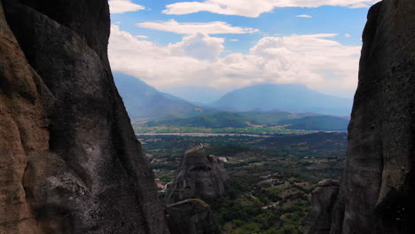 Unglaubliche-Aussicht-Auf-Die-Berge-Mit-Blauem-Wolkenhimmel-Im-Hintergrund,-Kleines-Dorf-Unten-–-Dolly-out,-Zwischen-Riesigen-Felsformationen-Hindurchfliegend