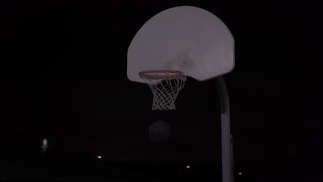 Teenage-girl-dribbles-basketball-then-shoots-it-in-the-net-at-an-outdoor-court-at-night