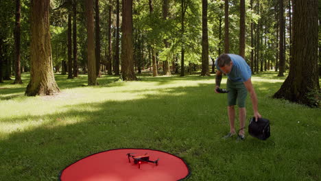 Man-flies-small-drone-in-a-park,-sunny-day,-static-shot