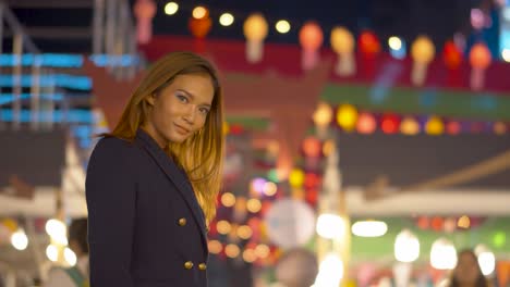 Attractive-young-woman-brushes-her-hair-back-and-smiles-at-the-camera-under-the-night-lights-in-the-city