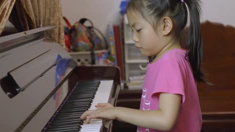 Side-view-of-child-Asian-girl-playing-piano-at-home,-practicing-piano-lesson