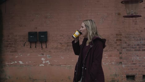 Young-Blonde-Female-Smiling-and-Walking-Down-the-Street-with-a-Coffee-in-Hand-During-the-Day-1
