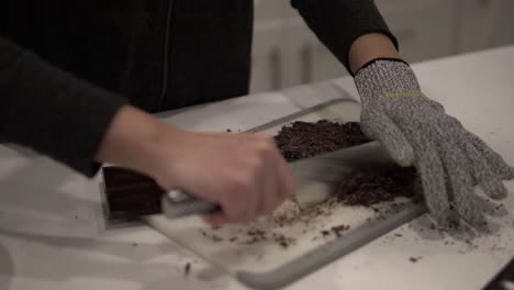 A-young-girl-cuts-up-dark-chocolate-before-melting-it-for-millionaire-shortbread-cookies-while-wearing-safety-gloves-1