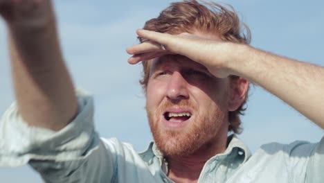 A-close-shot-of-the-face-of-a-ginger-haired-man-shading-his-eyes-looking-and-pointing-to-the-horizon