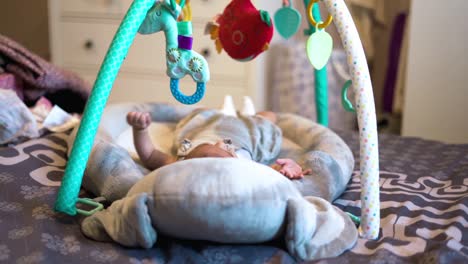 Cute-Newborn-Baby-Girl-Laying-in-Cradle-And-Curiously-Looking-At-Toys-Above-Her
