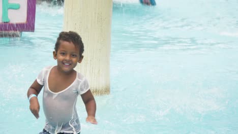 A-happy-mixed-raced-young-boy-exploring-a-children's-water-park-while-standing-under-spraying-water-and-running-and-laughing