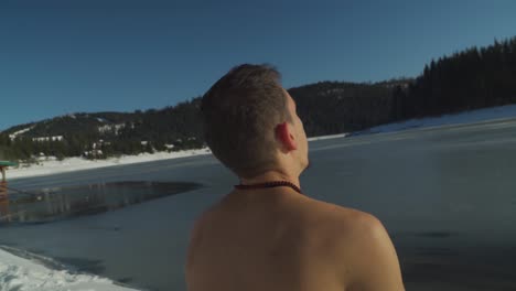 Hombre-Sin-Camisa-Sentado-En-La-Nieve-Junto-Al-Lago-Congelado-Respirando-Pesadamente-Mientras-Prepara-La-Mente-Y-El-Cuerpo-Para-Sumergirse-En-Agua-Helada