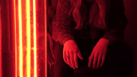 Porträt-Einer-Jungen-Kaukasischen-Frau,-Die-In-Einer-Bar-Mit-Orangeroter-Neonbeleuchtung-Sitzt